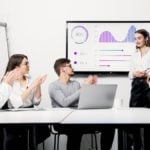 a group of people clapping to a woman presenting a graph on screen with success rate