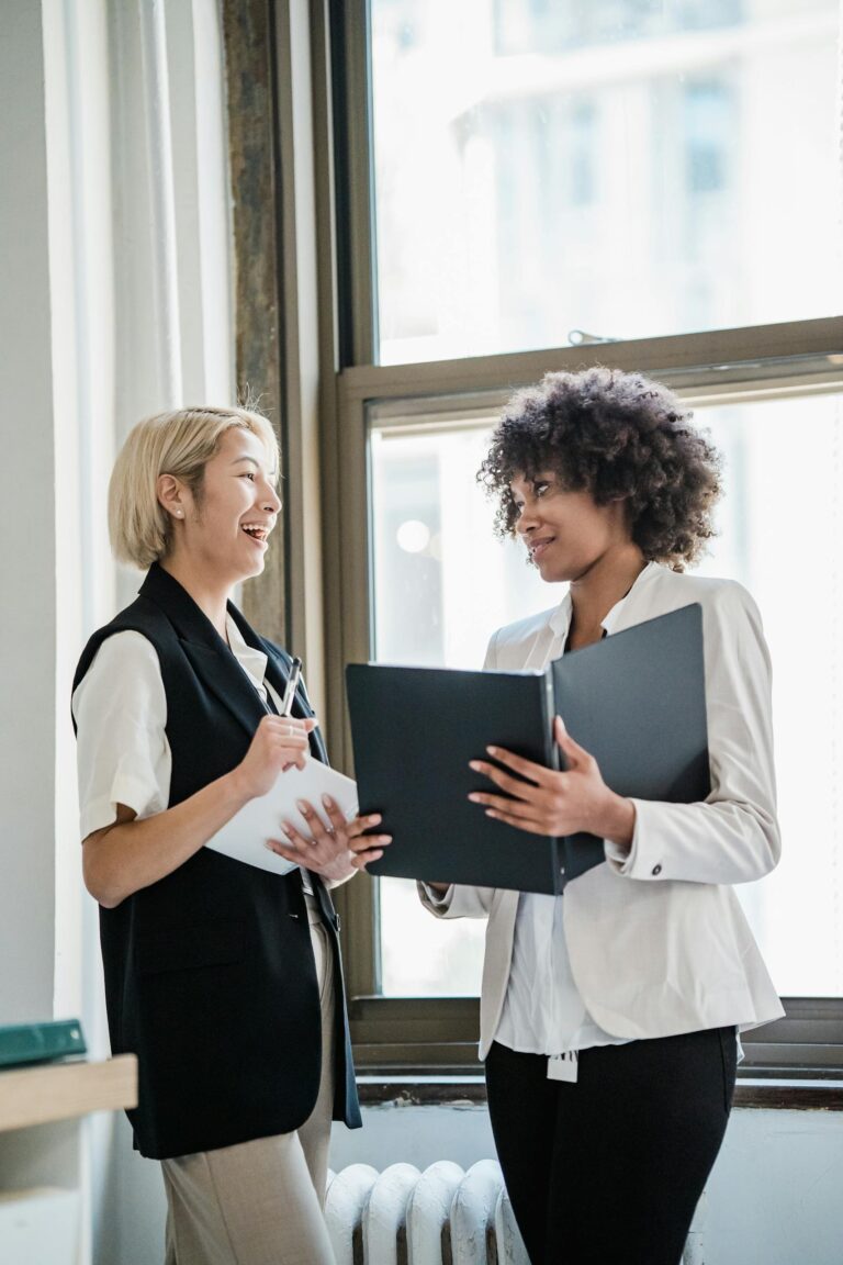 Two diverse businesswomen discussing documents in a bright office setting, highlighting teamwork and success.